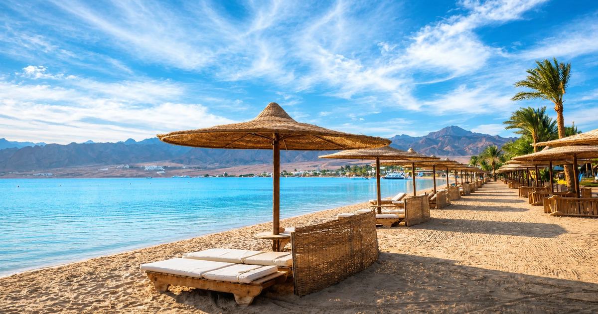 Red Sea beach with straw parasols, wooden sun loungers and rocky mountains in the background, Hurghada Egypt